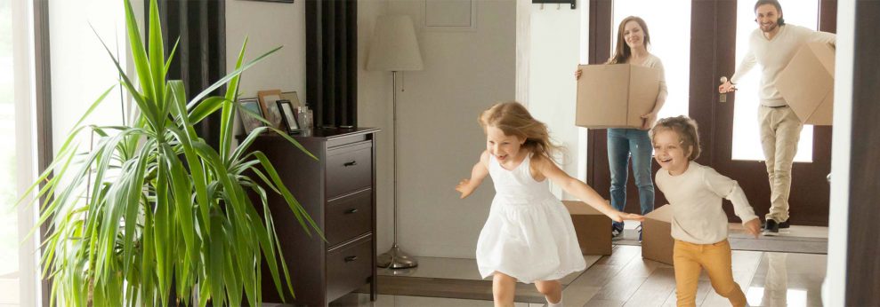 kids running through empty house as parents hold moving boxes